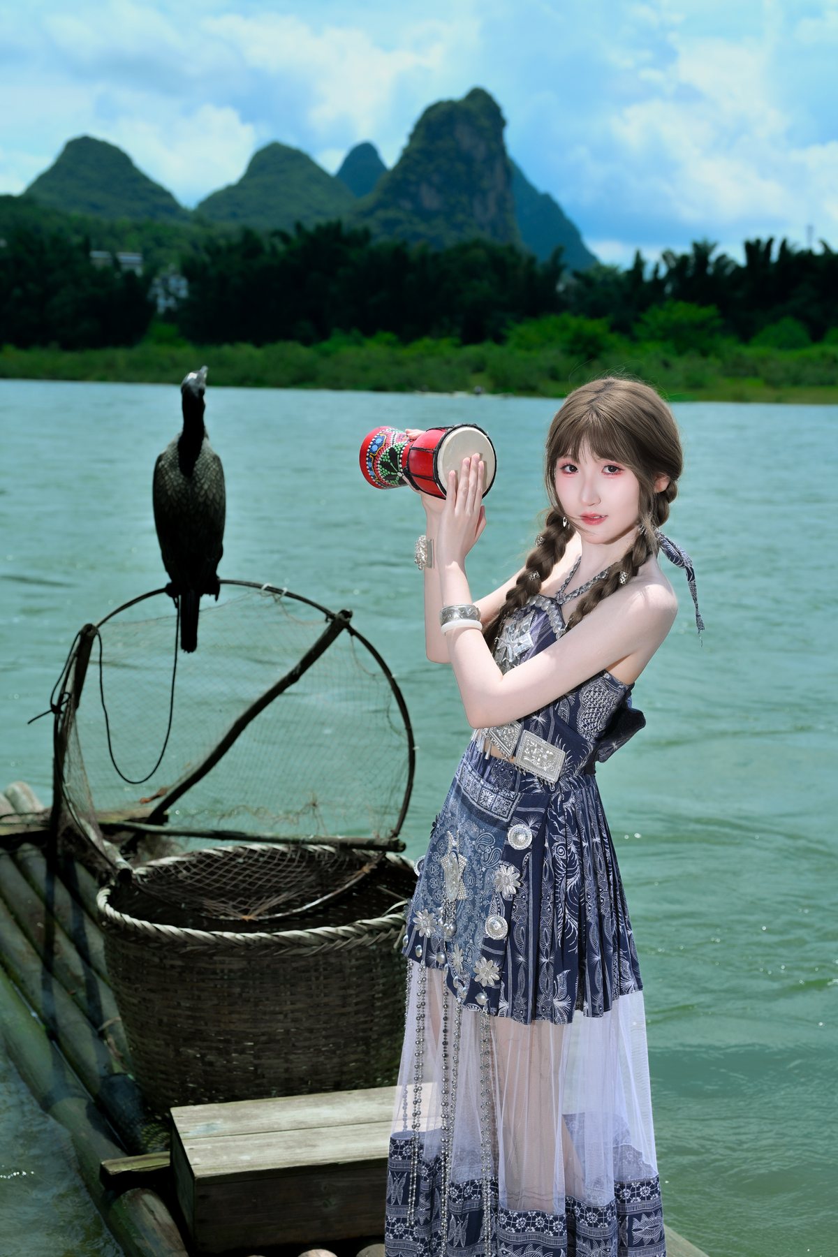 Cici holding a drum beside the river and cormorant prop